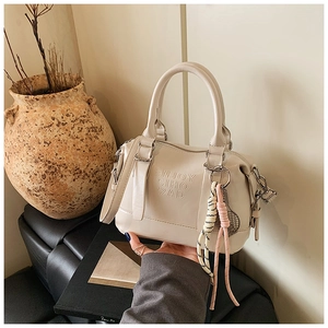 Detail of cream soft leather Boston bag featuring luxury embossed lettering and woven charm
