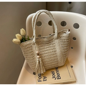 Detail of hand-woven straw tote bag with tassel accent on a minimalist chair