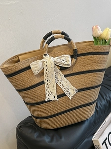 Artistic woven straw basket tote bag with contrasting black stripes and large white lace bow