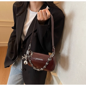 Détail d'un sac baguette en cuir marron brillant avec chaîne argentée et breloque lapin