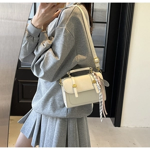 Detail view of cream leather square bag with golden clasp and decorative striped silk scarf