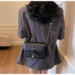 Detail of black crossbody bag featuring embossed floral patterns and a metal chain strap