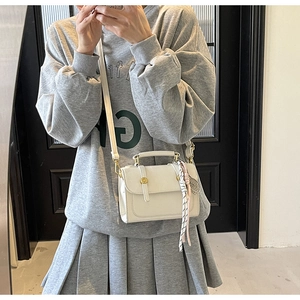 Detail of white mini square bag with golden lock and decorative black and white cord charm