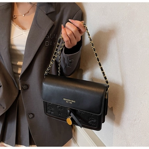 Detail of black textured crossbody bag with gold chain strap and tassel charm decor