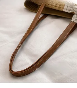 Detail of brown leather strap with white stitching on striped woven summer tote bag