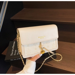 Close-up of cream square bag featuring embossed star patterns and gold chain strap