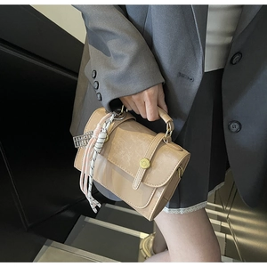 Detail of a beige square handbag with a gold round buckle and decorative silk scarf