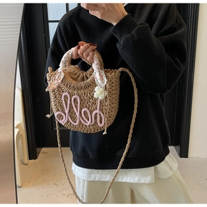 Detail of straw woven beach bag featuring pink hello lettering and floral scarf handle