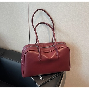 Close-up of deep red pebbled leather vintage shoulder bag resting on a leather sofa