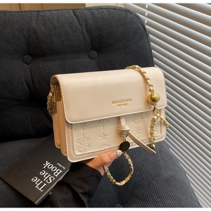 Detail of cream leather square bag featuring embossed star patterns and gold chain strap