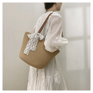 Straw woven tote bag with white lace bow and brown leather strap on model