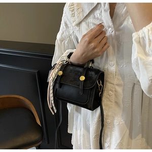 Detail of black crossbody bag with textured flap, gold button, and striped silk scarf accessory
