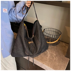 Detail of dark denim tote bag with drawstring closure and leather logo patch