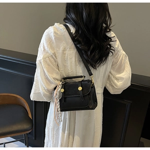 Detail of black leather crossbody bag with gold hardware and stylish tassel charm