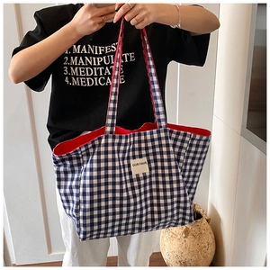 Detail of blue and white checkered canvas tote bag with 'OUR FAVE' patch on a model