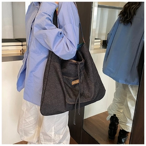 Detail of gray denim tote bag featuring a brand label and decorative drawstring closure