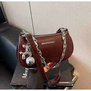 Détail du sac baguette en cuir verni bordeaux avec chaîne argentée et breloque chien