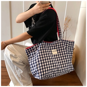 Detail of blue vichy tote bag with red handles and white square logo patch