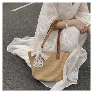 Detailed close-up of woven tote bag featuring white lace bow and brown leather handle