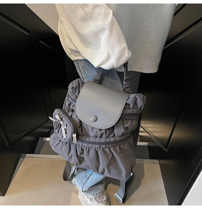 Detail of dark grey pleated backpack with smooth leather flap and mini bow charm