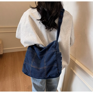 Detail of dark blue denim crossbody bag with contrast orange stitching on a model back