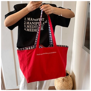 Detail of red canvas tote bag showing interior blue plaid lining and slogan print