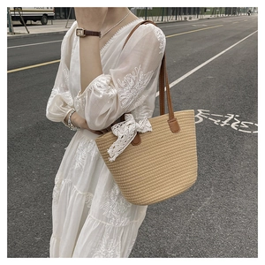 Detail of woven straw tote bag with lace bow and brown leather strap on white dress