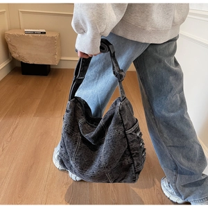 Detail of oversized washed denim crossbody bag with white stitching and frayed edges