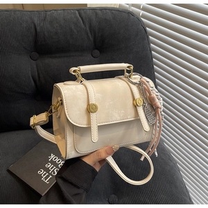 Detail of cream crossbody bag with metal buckle, heart charm, and silk scarf on a sofa
