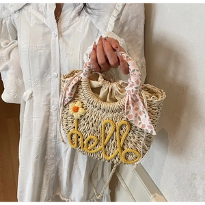 Detail of straw woven handbag featuring hello embroidery, yellow flower, and floral scarf