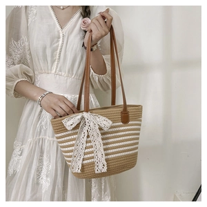 Detail of summer straw tote bag featuring white lace bow and brown leather strap