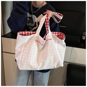 Close-up of a white canvas tote bag with red plaid lining and red slogan print detail