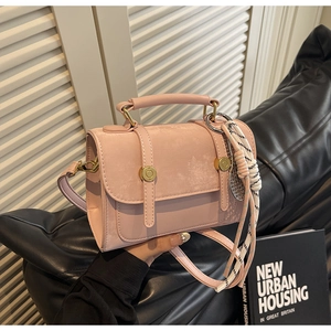 Detail view of pink leather handbag with suede flap and decorative silk scarf on sofa