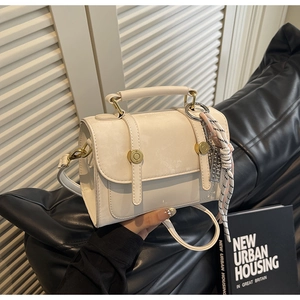 Close-up of cream leather square bag featuring gold buckles and braided rope charm detail