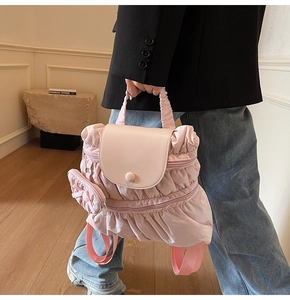 Pink pleated backpack with matching coin purse and leather flap, carried by a model