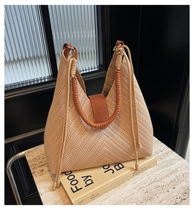 Detail of beige woven tote bag with brown cord handle and gold rings on a book
