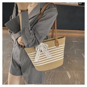 Detail of woven straw tote bag featuring white stripes, lace bow, and brown leather strap