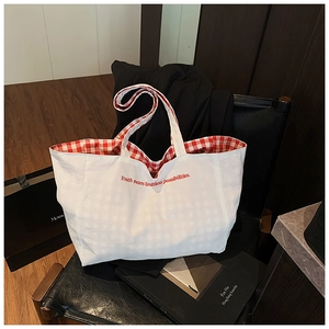 Detail of red embroidered text on a large white canvas tote bag with red checkered lining