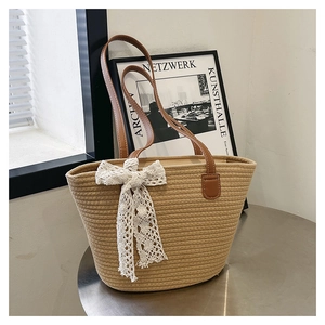 Detail of hand-woven straw tote bag with white lace bow and brown leather handles