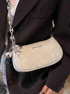 Sac demi-lune beige avec chaîne et breloque chien ballon, porté sur un blazer noir