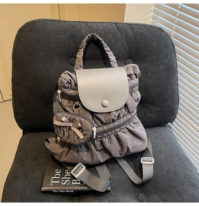 Detailed view of dark grey ruffle backpack with a leather flap and mini bow coin purse accessory
