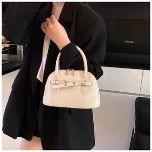 Detail of cream white shell handbag with glossy finish and metal buckles worn by model