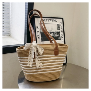 Close-up of woven tote bag featuring striped patterns and a white lace bow on metal table