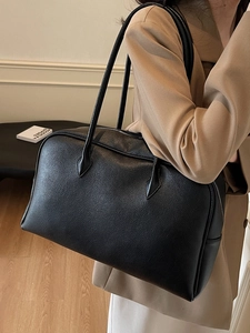 Minimalist black lychee leather shoulder bag with zipper closure shown on a female model
