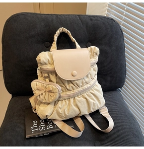 Detail of beige pleated backpack with heart-shaped bow charm on black velvet chair