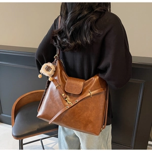 Detail view of brown vintage leather tote featuring crossbody straps and lion plush charm
