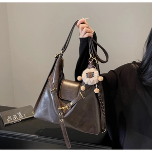 Detail of dark brown leather tote bag with gold metal buckle and cute plush charm pendant