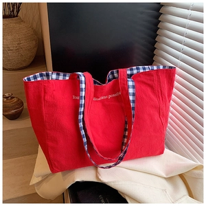Detailed view of red canvas tote bag with blue checkered lining and white embroidery