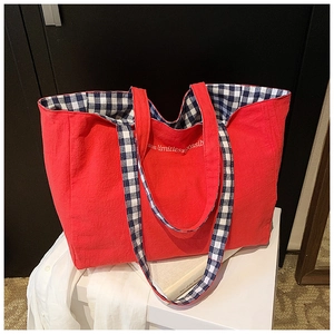 Close-up of red canvas tote bag with blue plaid lining and embroidered dream slogan