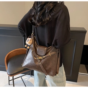 Detail showing vintage dark brown tote bag with metal buckles and a yellow plush charm